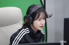 a young woman wearing headphones sitting in front of a computer monitor and looking off to the side