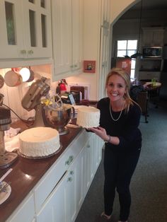 a woman standing in front of a counter holding a cake