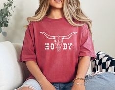 Yeehaw, cowgirls! Saddle up in style with this western-inspired oversized graphic tee. This shirt says howdy loud and proud, featuring a bold longhorn photo that will make you stand out at any rodeo, bachelorette party, country concert, or festival. Embrace your inner cowgirl and rock this statement piece that perfectly captures that western charm. Get ready to lasso some compliments in this must-have party shirt that combines cowgirl flair with a touch of edgy coolness. IMPORTANT: Please read all details below! We want you to be completely happy with your purchase 🌿 M A T E R I A L S  This is an adult unisex Comfort Colors T Shirt, made with 100% ring-spun cotton.  S I Z I N G  THIS T SHIRT IS UNISEX SIZING and is pre shrunk! If you are looking for the OVERSIZED look, please SIZE UP 1-3 Red Summer Top For Rodeo, Red Top For Summer Rodeo, Trendy Oversized Tops For Rodeo, Bachelorette Party Country, Rodeo Bachelorette Party, Nashville Party, Howdy Shirt, Rodeo Bachelorette, Shirts Trendy