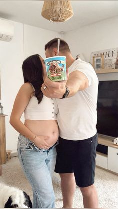 a man and woman standing next to each other in front of a tv holding a cup