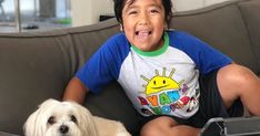 a young boy sitting on top of a couch next to a white dog with his tongue out