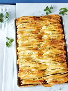 a casserole dish with potatoes and herbs on the side, ready to be eaten