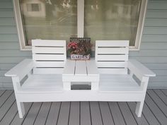 a white bench sitting on top of a wooden floor next to a window with flowers in it