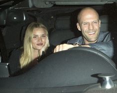 a man and woman sitting in the back seat of a car, smiling at the camera