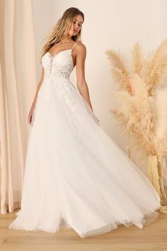 a woman in a white wedding dress standing on a wooden floor next to a plant