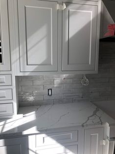 a kitchen with white cabinets and marble counter tops