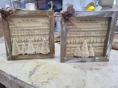 two wooden frames decorated with sheet music and christmas trees are sitting on a workbench