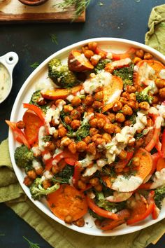 a white plate topped with lots of veggies and chickpeas covered in sauce