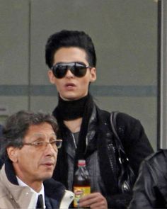 two men in black jackets and sunglasses standing next to each other, one holding a bottle