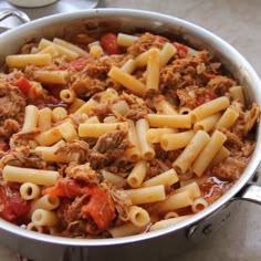 a pot filled with pasta and meat in tomato sauce on top of a table next to utensils