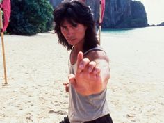 a man standing on top of a sandy beach pointing to the side with his finger