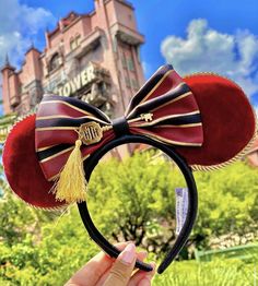 a person is holding up a minnie mouse ears headband in front of a castle