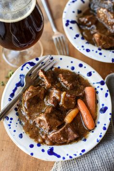 two plates filled with meat and carrots next to a glass of beer on a wooden table