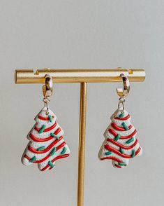 two christmas tree shaped earrings hanging from a gold hook - on earring stand against a white background