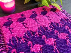 pink and purple crocheted rug with flamingos on it next to two candles