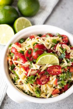 a white bowl filled with pasta salad next to limes