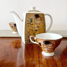 two cups and a teapot sitting on a wooden table next to a box with the painting's image painted on it