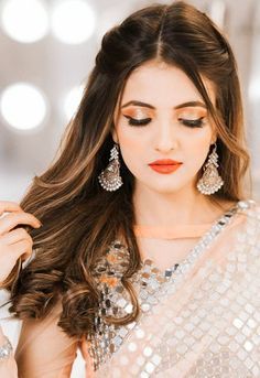 a woman with long brown hair wearing earrings and a white sari dress is looking down at her shoulder