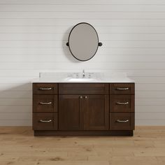 a bathroom vanity with a round mirror on the wall above it and wood flooring