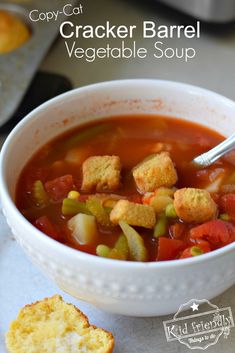 a white bowl filled with vegetable soup next to a piece of bread on top of a table