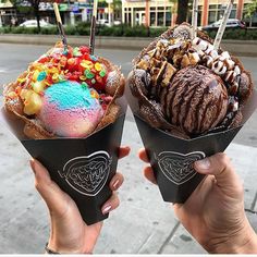 two people holding up ice cream cones with different toppings on them in front of a city street