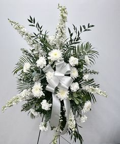 a bouquet of white flowers and greenery in a vase with a bow on the top