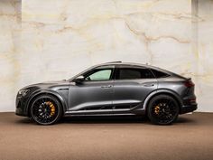 a grey car parked in front of a white wall with gold rims on it