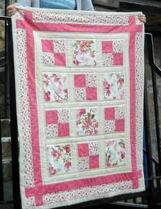 a woman holding up a pink and white quilt