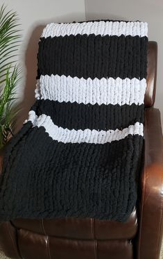 a black and white blanket sitting on top of a brown leather chair next to a potted plant