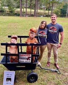 a man and two women standing next to a wagon with children dressed as dinosaurs in it