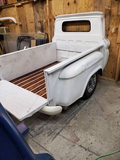 an old white truck parked in a garage next to a wooden wall and other tools