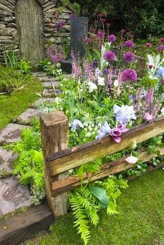 a garden filled with lots of flowers next to a stone wall and wooden bench in the grass