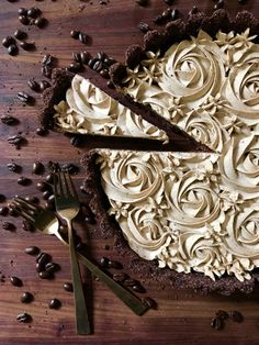 a chocolate cake with white frosting on a wooden table next to forks and coffee beans