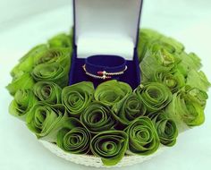 a ring sits on top of a bouquet of green flowers in a white basket with a blue velvet box