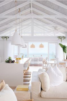 a living room filled with white furniture and lots of windows next to the ocean in front of it