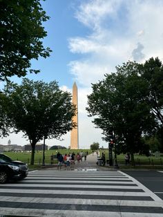 people are walking across the street in front of the washington monument, which stands tall