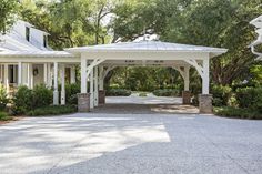 a white gazebo sitting in the middle of a driveway surrounded by trees and bushes