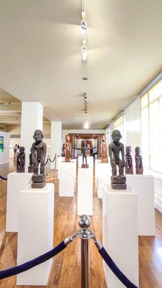 an art gallery with sculptures on pedestals and ropes in front of the room's windows