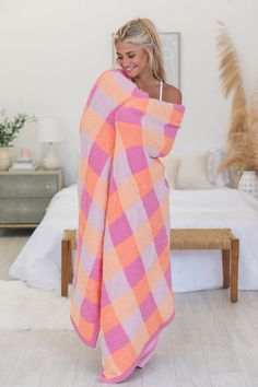 a woman wrapped in a pink and orange checkered blanket standing on a white bed