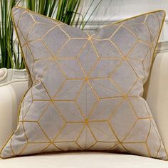 a white and gold pillow sitting on top of a couch next to a potted plant