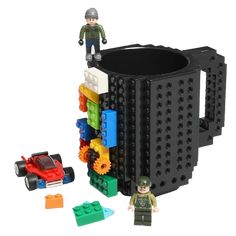 a black coffee mug with legos on it and a toy car next to it