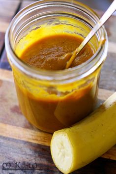 a jar filled with sauce next to a banana on top of a wooden cutting board