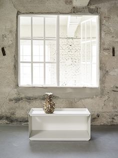 a white shelf sitting in front of a window next to a wall with a vase on it