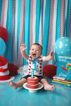 a baby boy sitting on top of a cake with his hands in the air and smiling