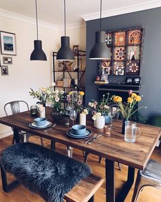 a dining room table with plates and bowls on it, flowers in vases at the end