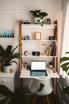 a laptop computer sitting on top of a white desk next to a potted plant