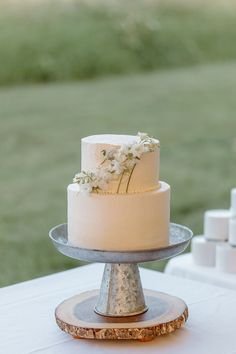 a white wedding cake sitting on top of a wooden stand next to a green field