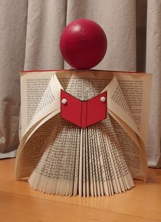 an origami book with a red ball on top sitting on a wooden table