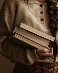 a woman holding two books in her hands and looking down at the book she is holding