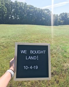 a hand holding a sign that says we bought land 10 - 4 - 19 in front of some trees